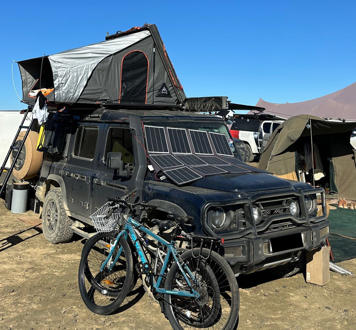 Overlanding 4x4 vehicle with rooftop tent and solar panel mounted on the bonnet at a bush campsite, with mountain bikes parked in front