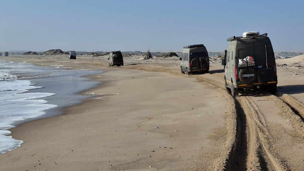 Three vans on a sandy beach with ocean waves in the background